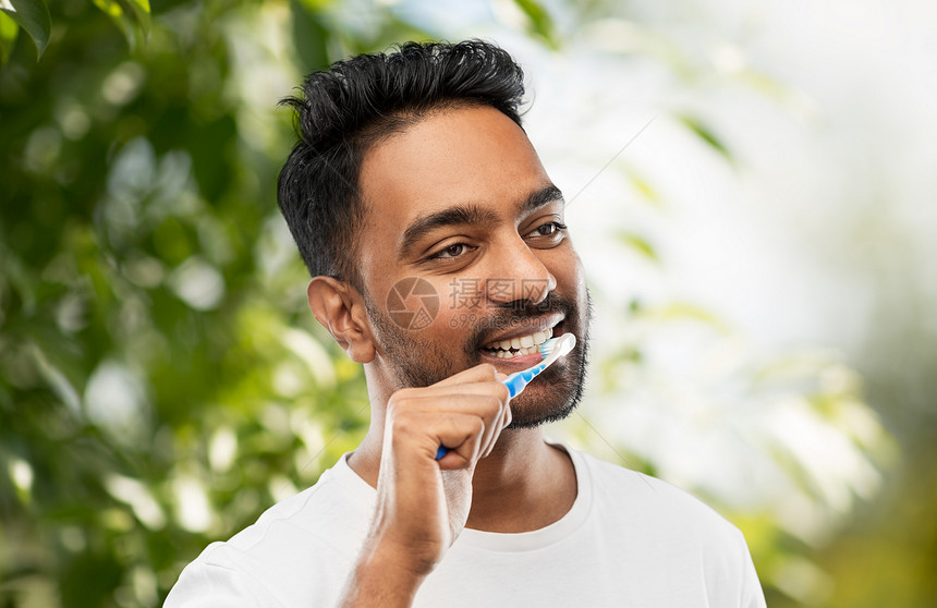 口腔护理,牙科卫生人的微笑的轻印度男子牙刷清洁牙齿的绿色自然背景印度男人带着牙刷清洁牙齿图片