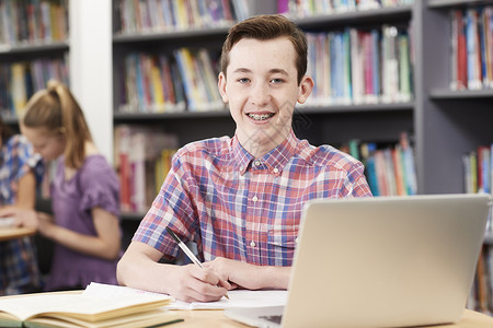 图书馆笔记本电脑上工作的男高中生的肖像图片