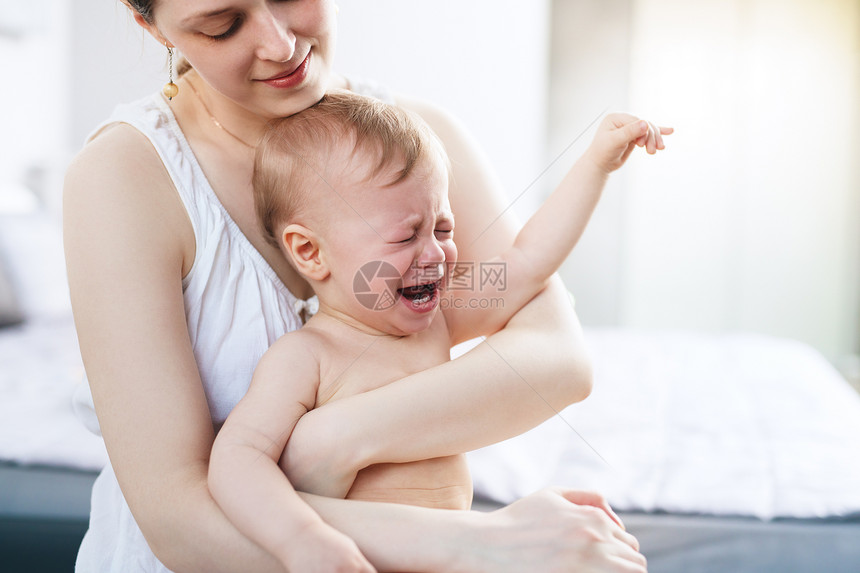 轻的女人手上着哭泣的婴儿明亮的白色图片