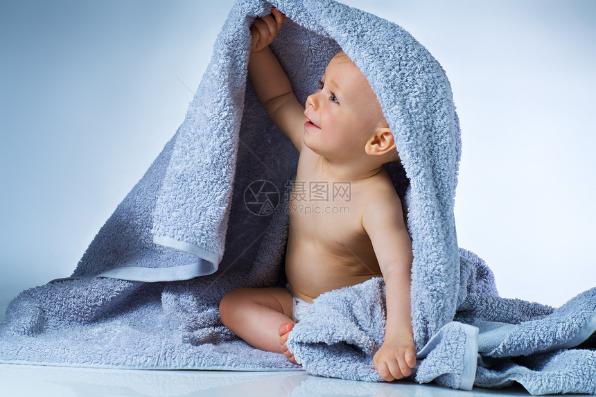 八个月后,婴儿洗完后坐柔软的大毛巾上,白色蓝色的背景上微笑图片