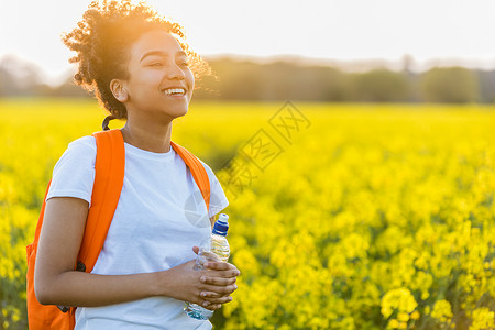 户外肖像美丽,快乐,欢笑,混合种族,非裔美国女孩,十几岁的女青,用水瓶金色的傍晚阳光下,片花田里喝水图片