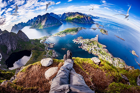 人称视角拍摄个徒步旅行者坐悬崖边缘的洛福滕个群岛诺德兰县,挪威鱼眼镜头背景图片