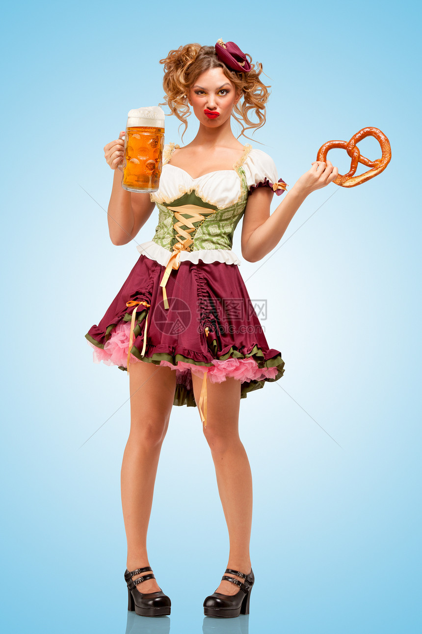 轻感的啤酒节女服务员穿着传统的巴伐利亚连衣裙,戴着个椒盐卷饼啤酒杯,蓝色背景上着脸图片