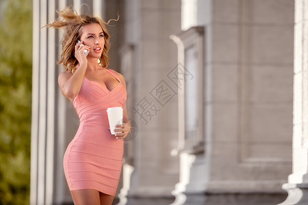 个穿着粉红色连衣裙的漂亮女人手机说话,着咖啡杯图片