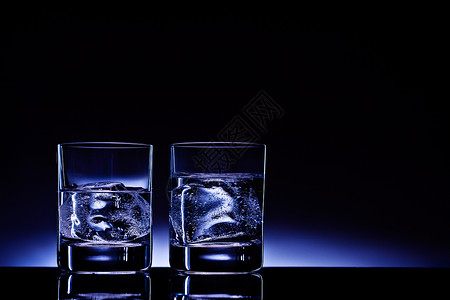 两杯伏特加加冰块,背景深蓝色的辉光背景图片