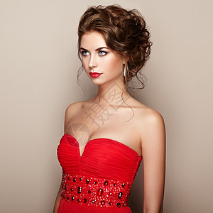 穿着优雅红色连衣裙的美丽女人的时尚肖像着优雅发型珠宝的女孩图片