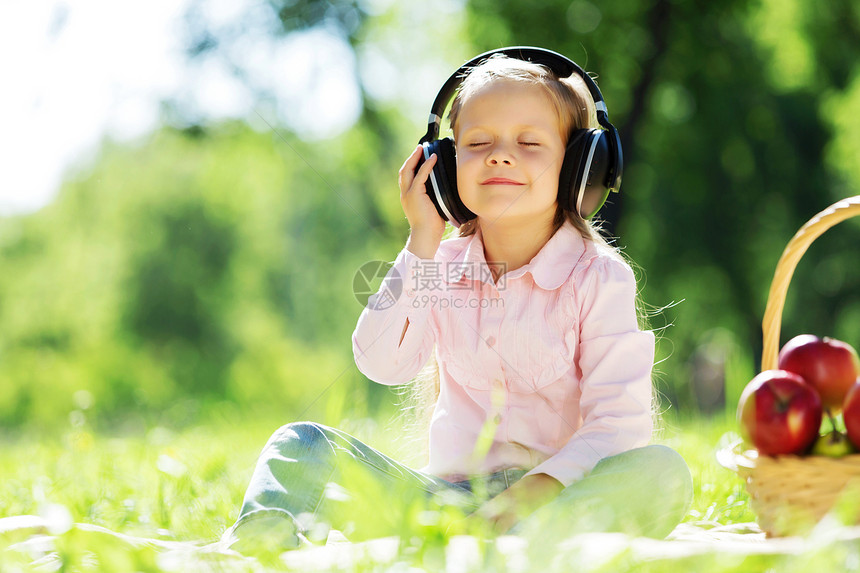 可爱的女孩戴着耳机坐夏天的公园里大自然的声音图片