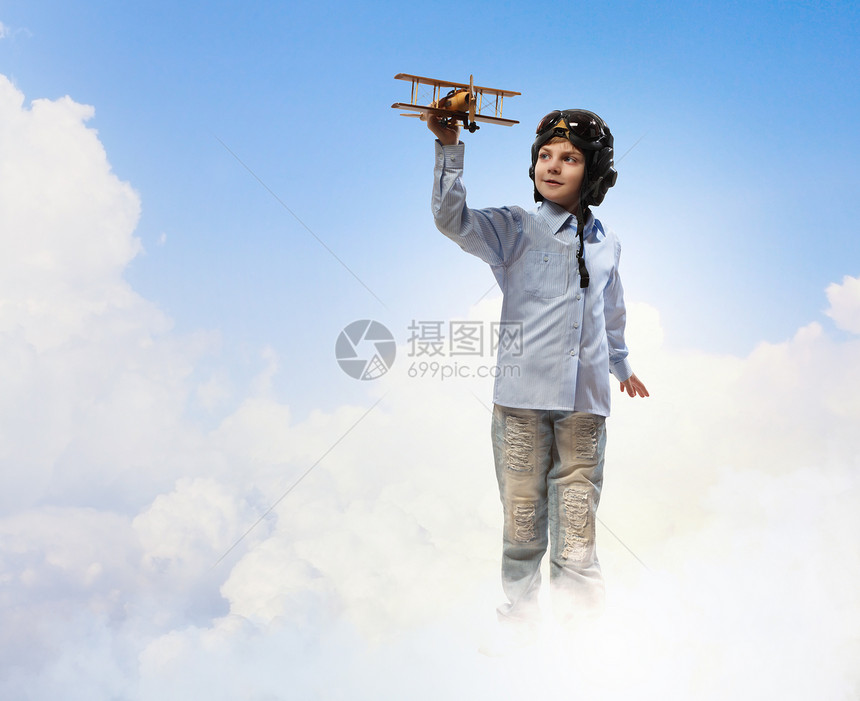 飞行员头盔中的小男孩云背景下玩玩具飞机的形象图片