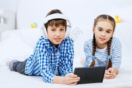 可爱的孩子平板电脑上玩游戏男孩女孩躺地板上用平板电脑图片