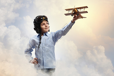 飞行员头盔中的小男孩云背景下玩玩具飞机的形象背景