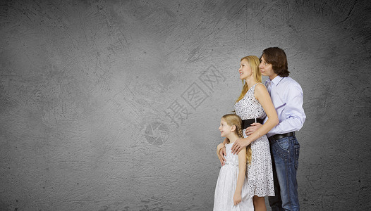 家三口幸福的家庭,父母女儿靠水泥墙背景图片