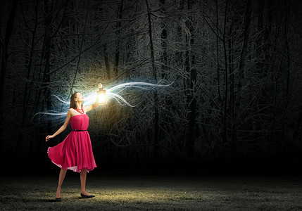 带灯笼的女人穿着红色连衣裙的轻女人走夜间的树林里背景图片