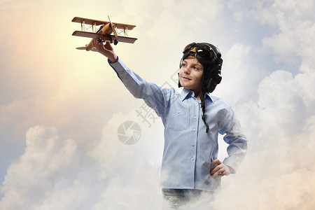 飞行员头盔中的小男孩云背景下玩玩具飞机的形象背景