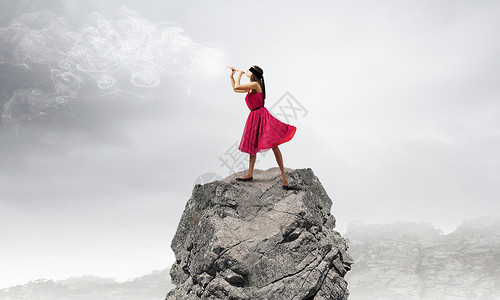 长笛的女人穿着红色连衣裙的轻女人岩石上玩Fife图片