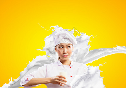 亚洲女厨师抗牛奶飞溅亚洲女厨师牛奶溅红色围裙上的彩色背景,着杯牛奶图片