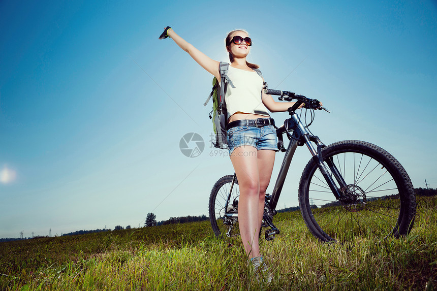 你积极的生活方式轻的运动女孩,背包骑自行车沿路边图片