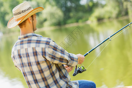 夏天钓鱼戴帽子的年轻人坐桥上钓鱼图片