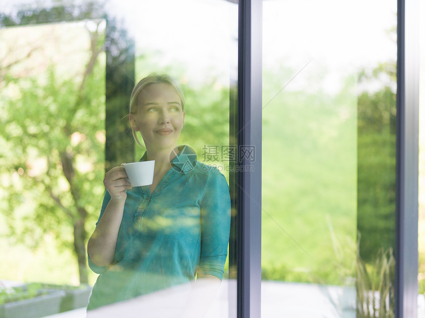 美丽的轻女人家里的窗户边喝早咖啡图片
