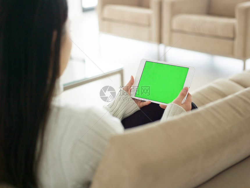 轻快乐的亚洲女人坐沙发上用数字平板电脑图片