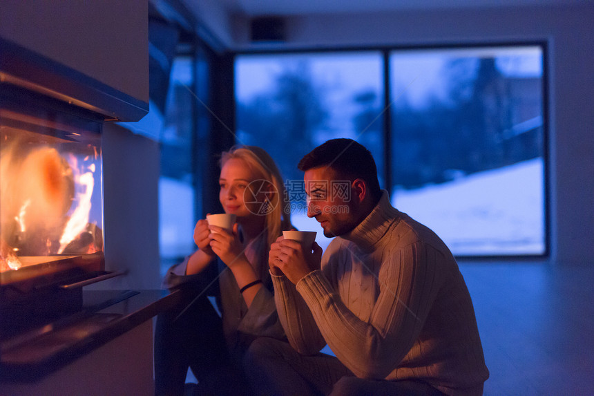 轻的浪漫夫妇坐壁炉前的地板上,寒冷的冬天晚上家里喝茶聊天图片