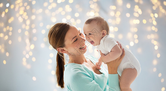 家庭,母亲,孩子父母的快乐的微笑轻母亲与小婴儿假期灯光背景图片