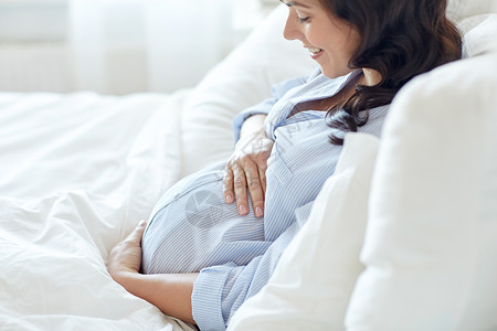 怀孕,休息,人期望的快乐微笑的孕妇躺床上,触摸她的肚子家里背景图片