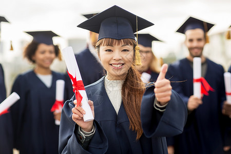 教育毕业手势人的群快乐的国际学生穿着灰浆板学士服,毕业证书竖大拇指微笑高清图片素材