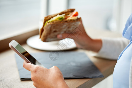食物,晚餐,技术人的女人与智能手机吃鲑鱼帕尼尼三明治与西红柿奶酪餐厅图片