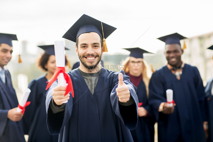 教育毕业手势人的群快乐的国际学生穿着灰浆板学士服,毕业证书竖大拇指