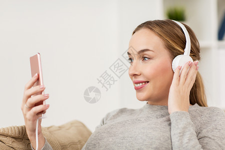 休闲,技术人的微笑的女人与智能手机耳机听音乐家家里智能手机耳机的女人图片
