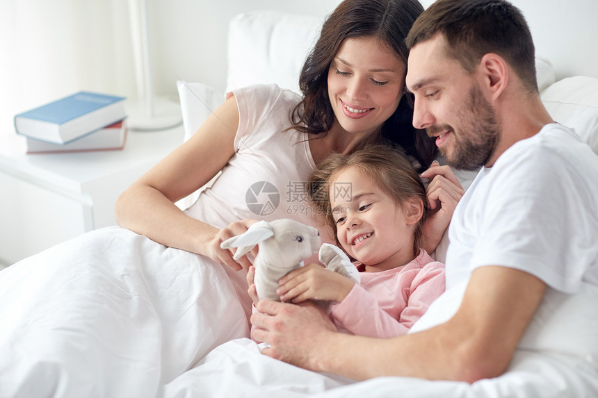 人,家庭早晨的快乐的孩子与玩具兔子父母床上家快乐的孩子玩具父母家里睡觉图片