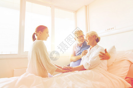 重阳节看望父母医学,支持,家庭保健人的快乐的老人轻的女人拜访欢呼她的祖母躺医院病房的床上幸福的家庭医院看望老妇女背景