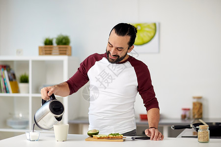 素食,健康饮食,人饮食男人用水壶泡茶,家里厨房吃蔬菜三明治带水壶的男人家早餐茶背景图片