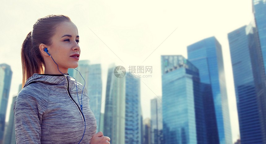 健身,运动,人,技术生活方式的快乐的女人跑步听音乐耳机新加坡城市摩天大楼的背景快乐的女人带着耳机城市里奔跑图片