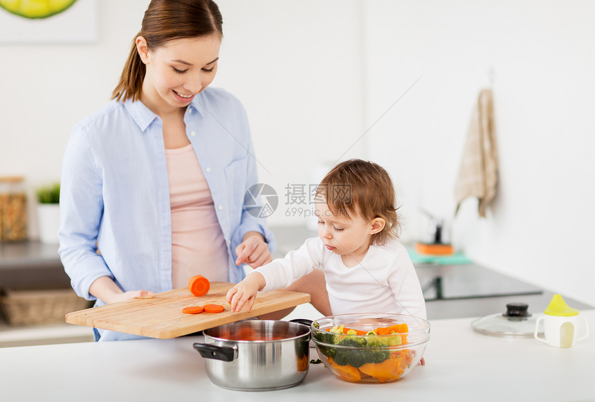 家庭,食物,健康的饮食,烹饪人们的快乐的母亲与切碎的胡萝卜小女婴与蔬菜锅家里厨房快乐的母亲婴儿家厨房饭图片