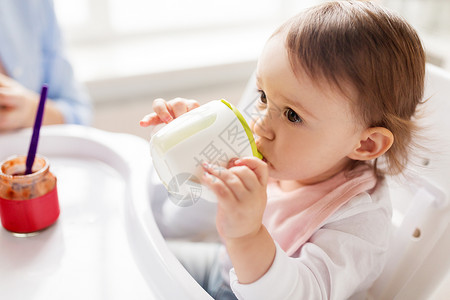 小孩喝果汁童人们的小婴儿喝喷口杯坐高椅子家里婴儿家里的高椅子上喷口杯里喝水背景
