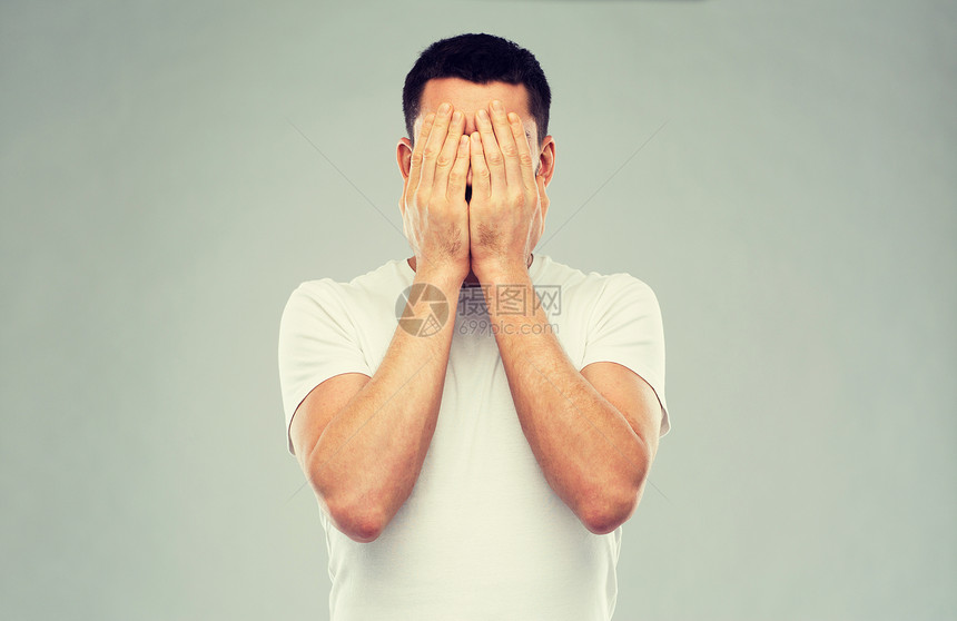 人,危机,情绪压力的男人穿着白色T恤,双手覆盖灰色背景上穿着白色T恤的男人用手遮住脸图片