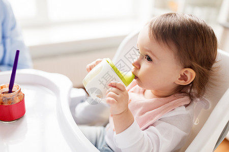 小孩喝果汁童人们的小婴儿喝喷口杯坐高椅子家里婴儿家里的高椅子上喷口杯里喝水背景