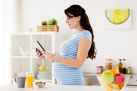 健康饮食,怀孕人的孕妇与平板电脑家里厨房吃早餐孕妇家里吃平板电脑图片
