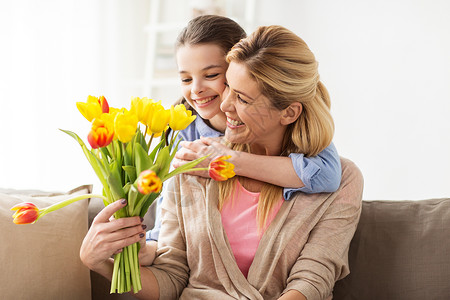 惊喜令人愉快的人,家庭假期的快乐的女孩送郁金香花拥抱她的母亲家里快乐的女孩家里给妈妈送花背景