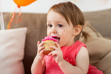 快乐的女婴在生日聚会上吃纸杯蛋糕图片
