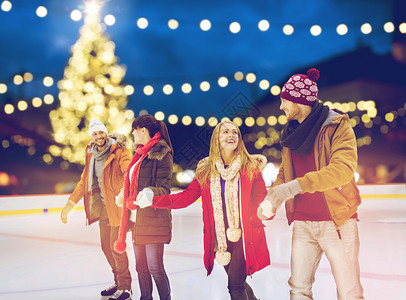 诞节,冬天休闲的快乐的朋友户外假日灯光背景下牵手溜冰场诞滑冰场的快乐朋友背景图片