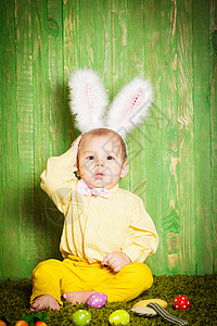 男孩和兔小男孩像复活节兔子样草地上放着五颜六色的鸡蛋复活节兔子蹒跚学步背景