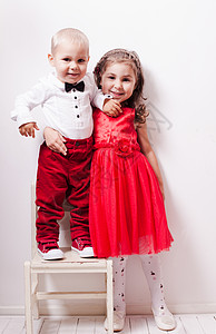 穿着红色裤子的小男孩穿着红色连衣裙的女孩谐地摆出照片的姿势图片