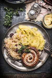 烤香肠与土豆泥酸菜金属板与餐具服务黑暗的乡村桌子,顶部视图,德国传统食品图片