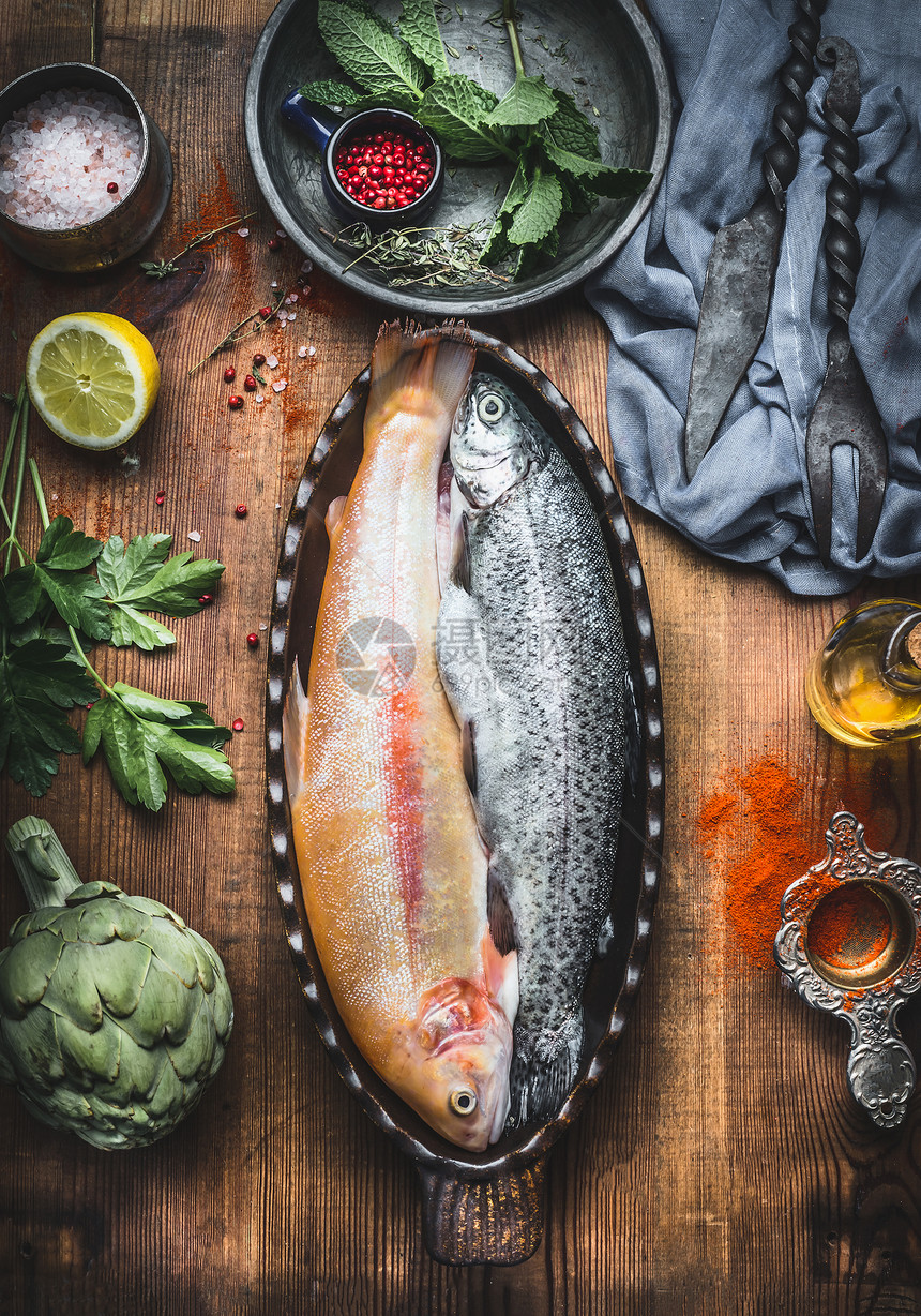 鱼盘烹饪准备两条鳟鱼以烘焙的形式出现木制乡村厨房桌子的背景上,蔬菜调味品的成分,风景图片