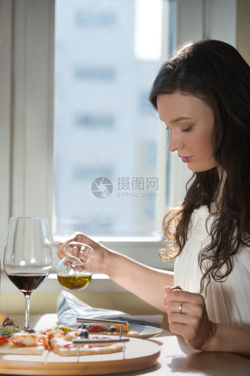 美丽的轻女人家吃自制披萨喝红酒图片