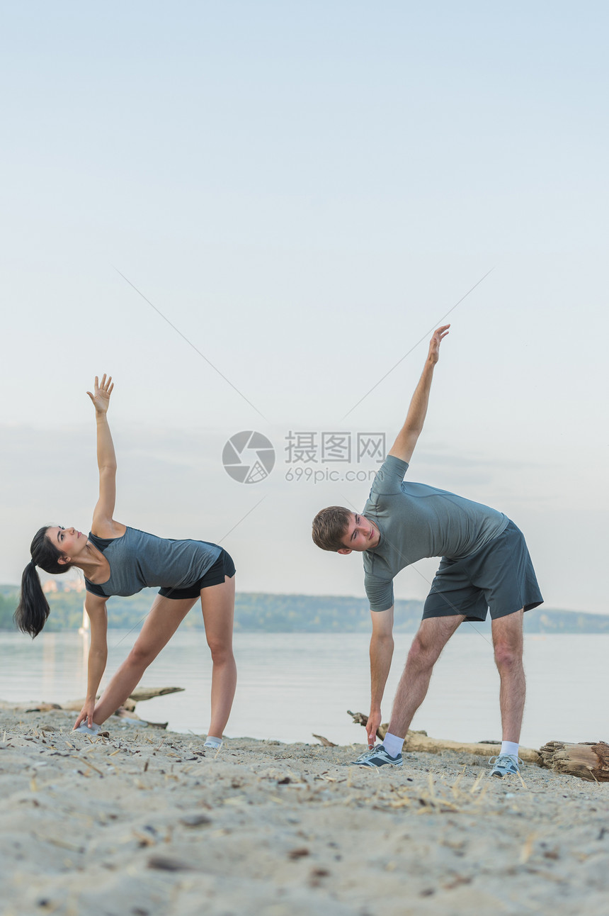 健身,运动,友谊生活方式的微笑的夫妇海滩上伸展瑜伽练早上图片