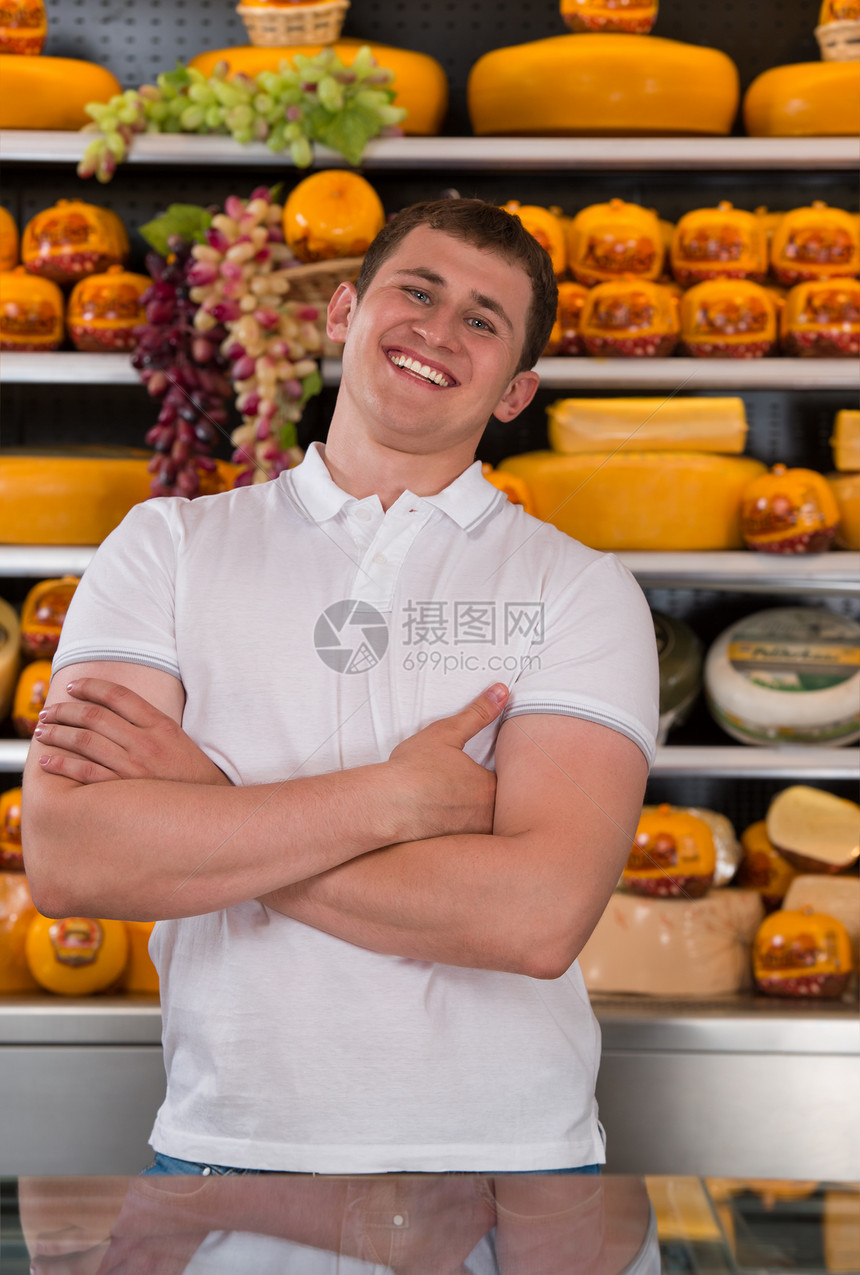 家奶酪商店的英俊的男主人站那里,双臂交叉,带着自信的微笑看着相机图片