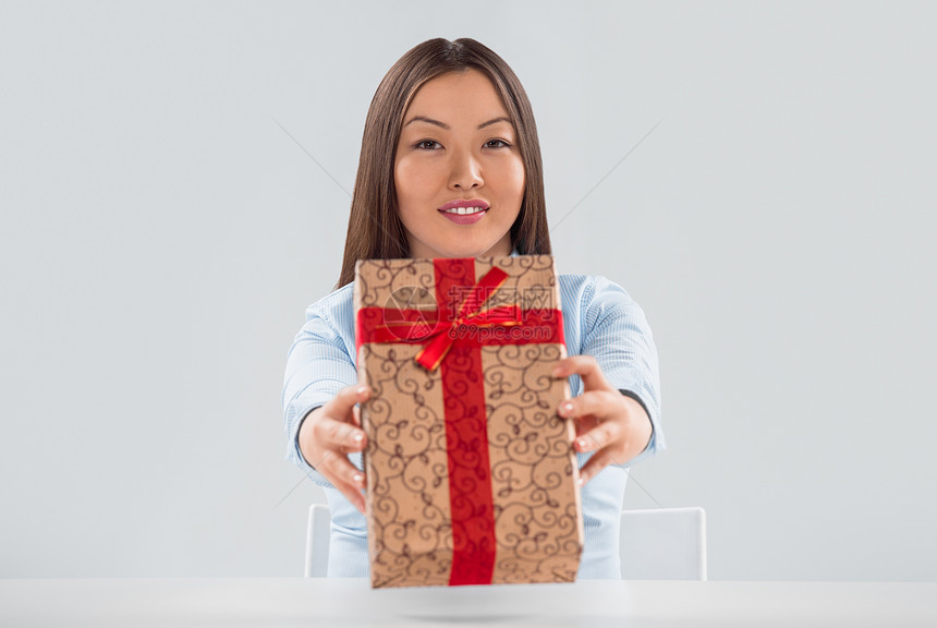 轻的商业女人坐她的桌子上着个礼品盒的肖像图片